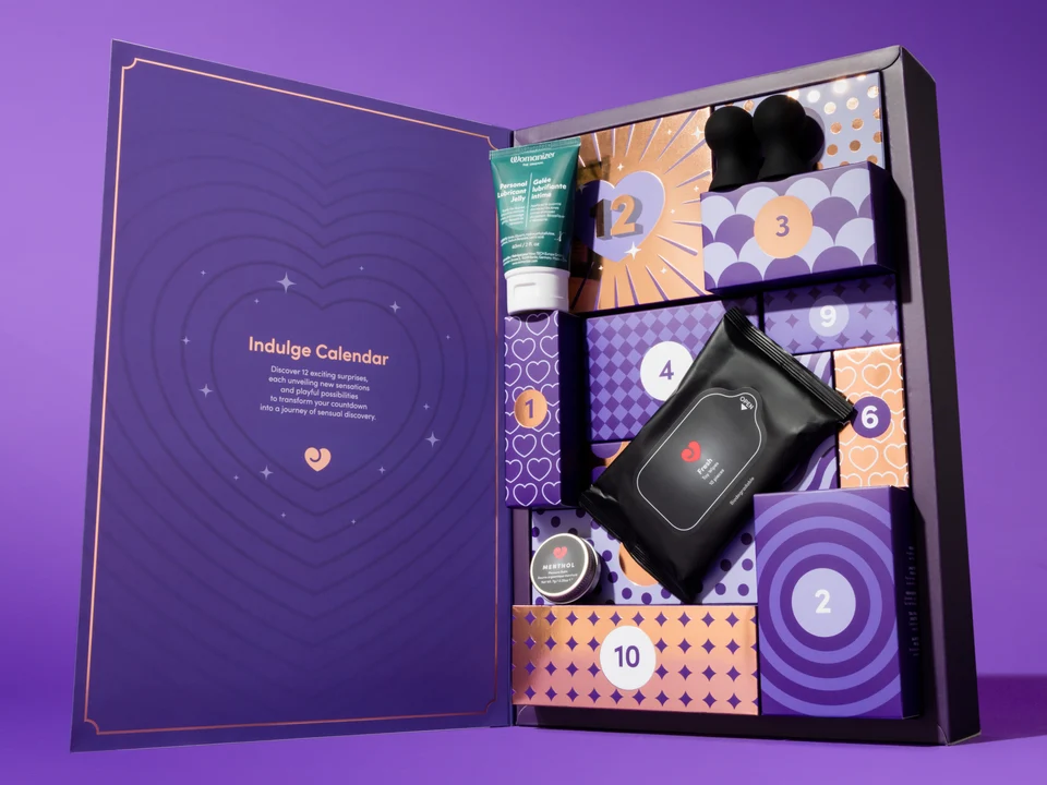 Lovehoney Indulge Advent Calendar 2026 (12 Day) product image Open purple Lovehoney Indulge 12-Day Advent Calendar box displaying numbered drawers, a tube of Womanizer lubricant, and a packet of Lovehoney Fresh Toy Wipes against a solid purple background